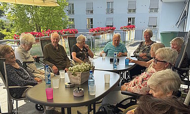 Die Bewohnerinnen und Bewohner genießen die Zeit auf dem Balkon.