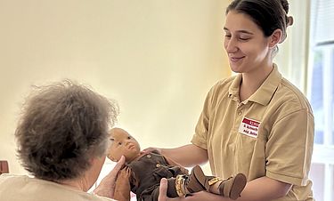 Svenja Schmidtke-Krohn reicht einer demenziell erkrankten Bewohnerin die Babypuppe, durch deren Gewicht die Seniorin ihren Körper wieder besser spüren kann. 